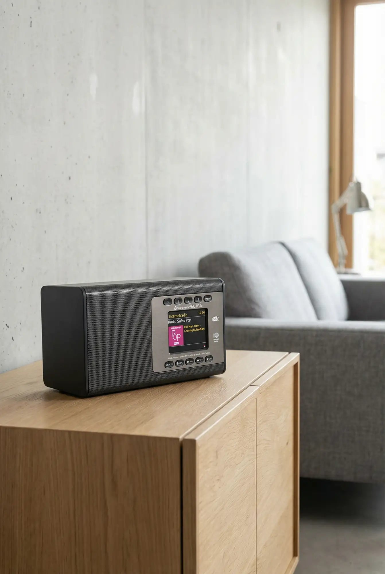 Schwarzes rechteckiges digitales Radio mit texturiertem Vorderpanel und silbernen Bedienknöpfen, das rosa Bildschirmgrafiken anzeigt.